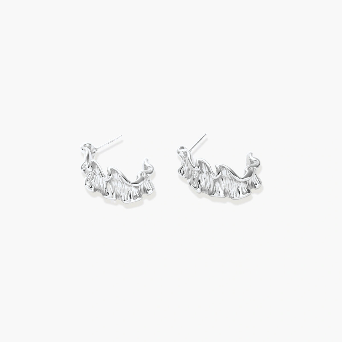 Textured white gold-plated hoop earrings with flowing wave pattern against cream background, showing dimensional rippled surface.