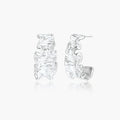 Textured white gold-plated hoop earrings with flowing wave pattern against cream background, showing dimensional rippled surface.