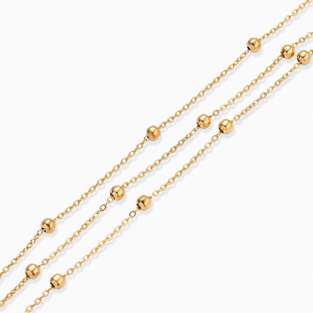 Three-strand gold-plated bracelet with clustered ball beads and adjustable clasp on cream background