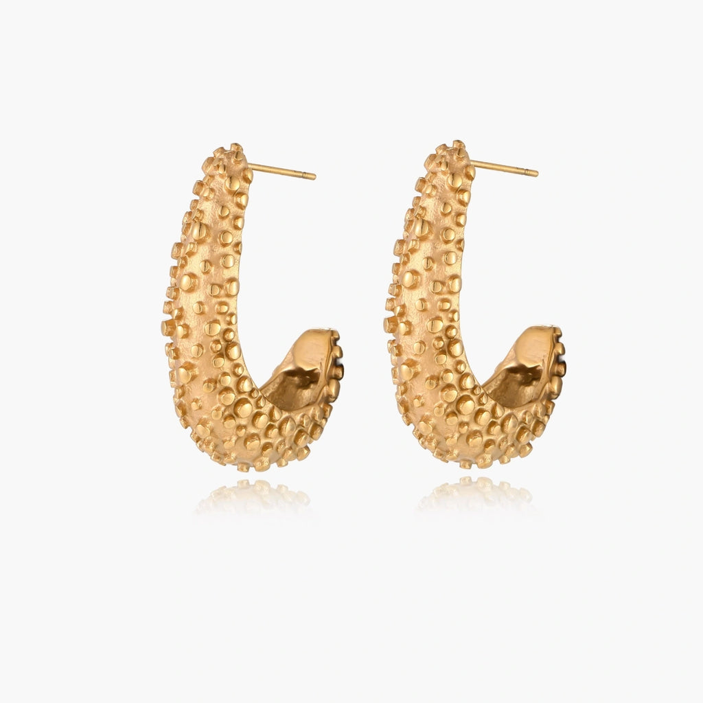Curved gold hoop earrings with raised granulated texture resembling sea urchin surface on cream background