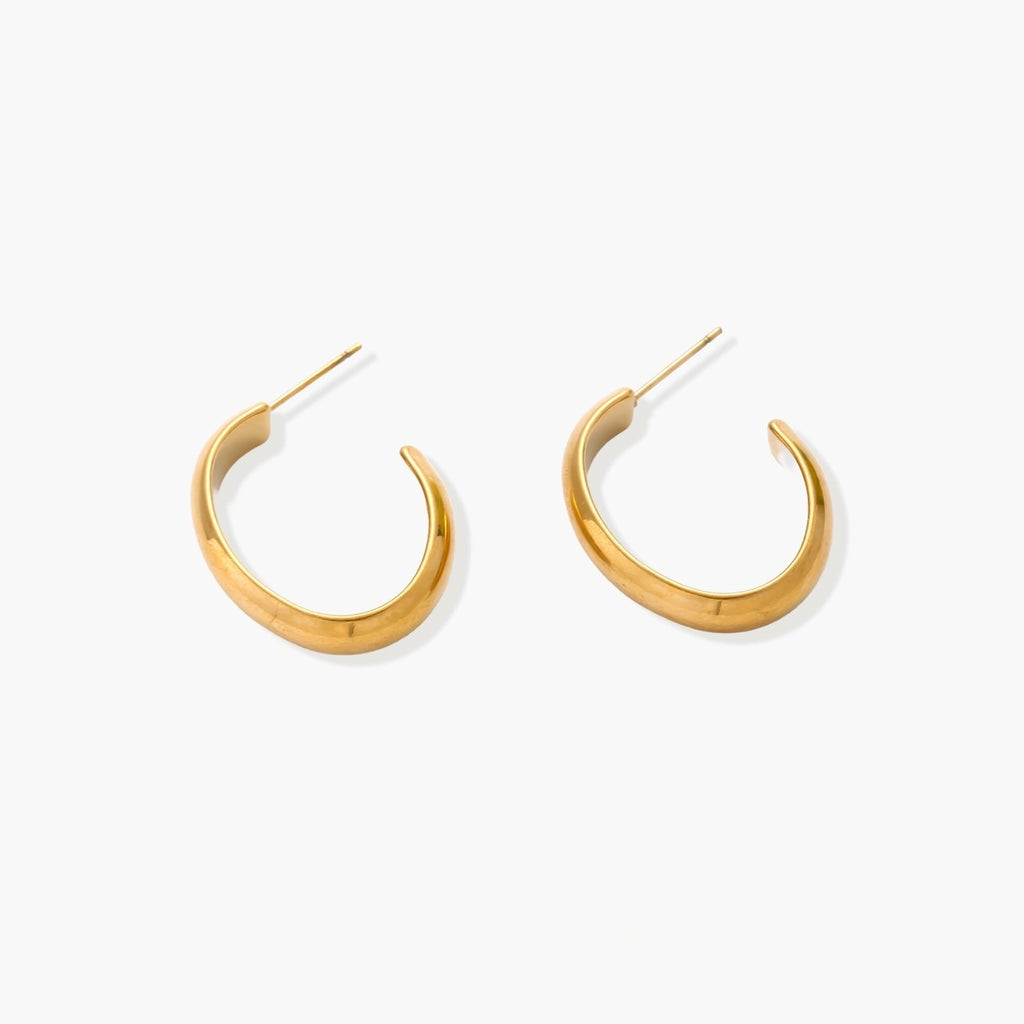 Chunky tubular hoop earrings in warm 14K gold-plated finish with smooth polished surface on cream background.